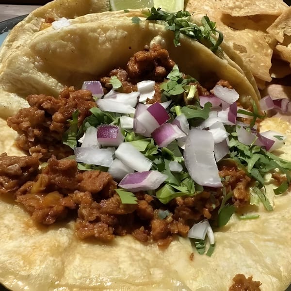 Close-up of a La Familia Cafe taco with seasoned meat, cilantro, and diced red and white onions.