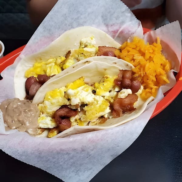 Two breakfast tacos with scrambled eggs, sausage, rice, and refried beans in a red basket.