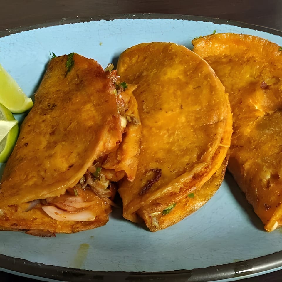 Three golden-brown birria tacos with meat, onions, and cilantro, served with lime wedges on a blue plate.