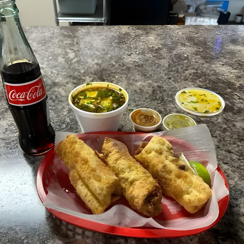 Three golden-fried flautas in a red basket with lime, a Coca-Cola, soup, and sauces.