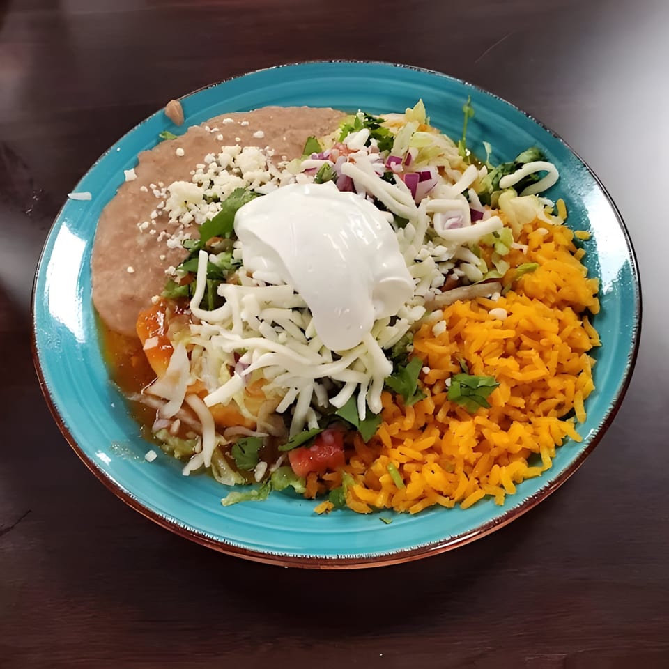 A vibrant Mexican combo plate with refried beans, rice, enchiladas, and fresh toppings on a blue plate.