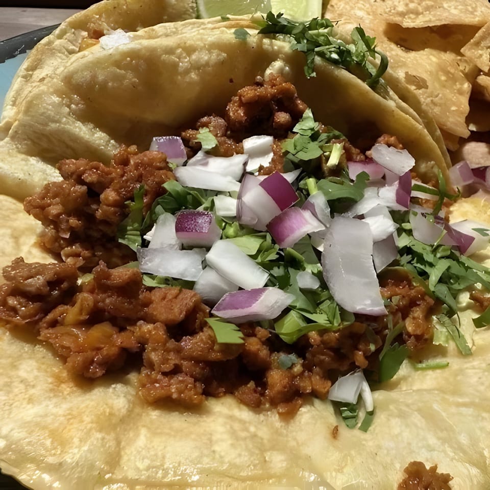 Close-up of a La Familia Cafe Mexican taco with seasoned meat, cilantro, and diced onions.
