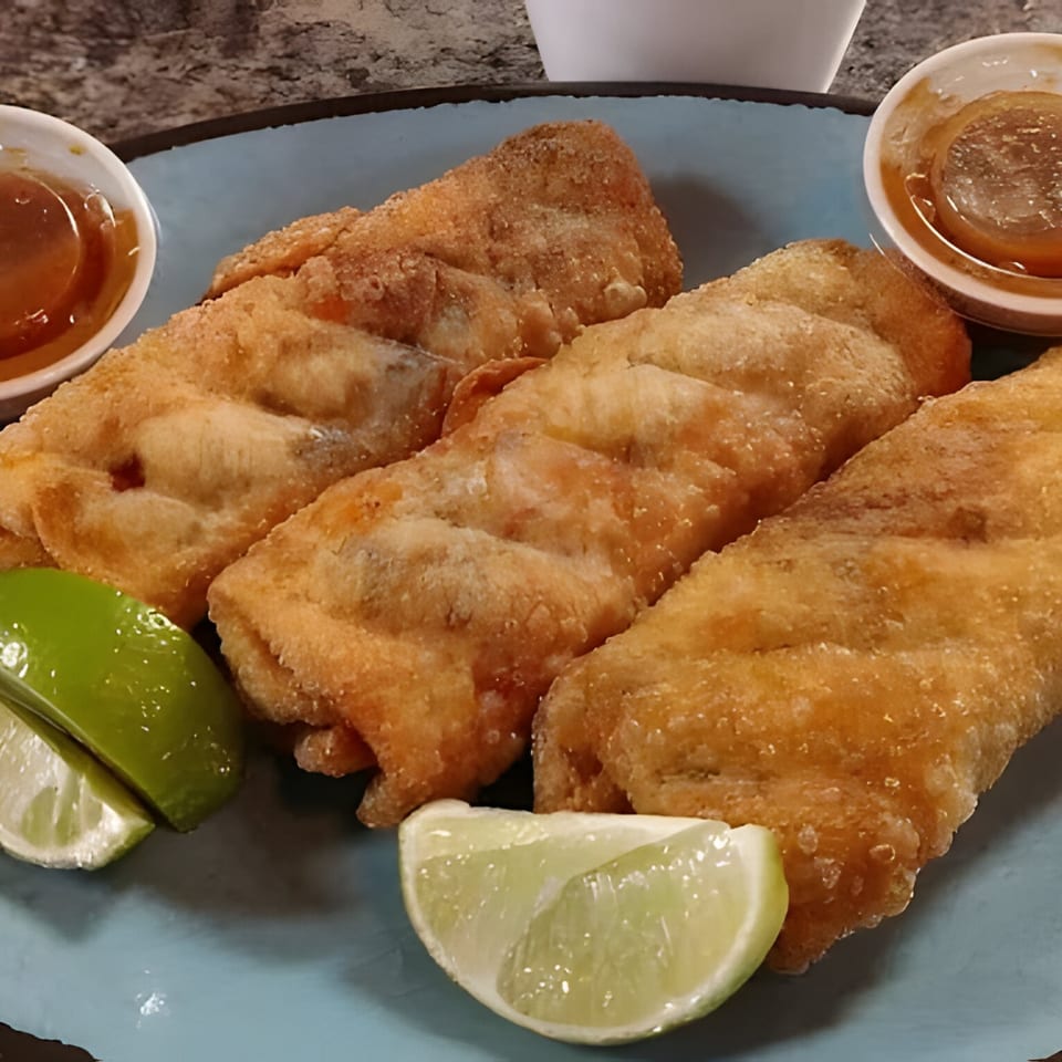 Three golden-brown fried taquitos with lime wedges and two small cups of sauce on a blue plate.