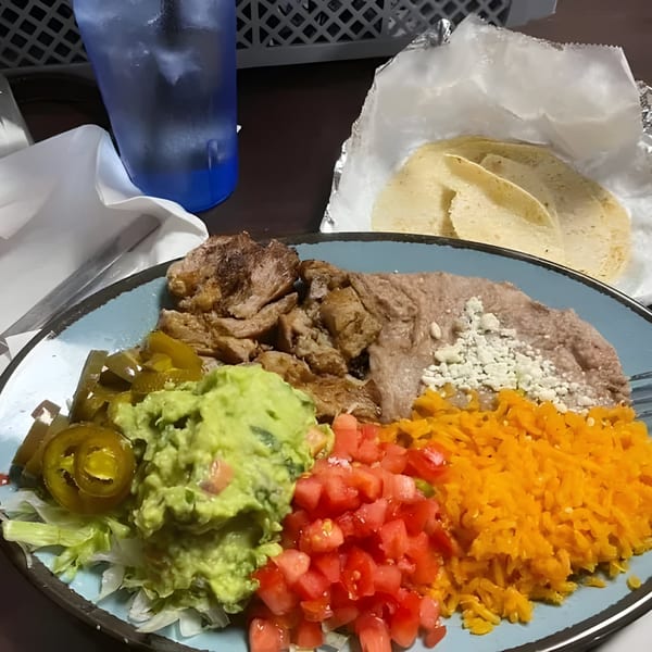 A Mexican dish with meat, refried beans, rice, guacamole, diced tomatoes, and jalapeños.