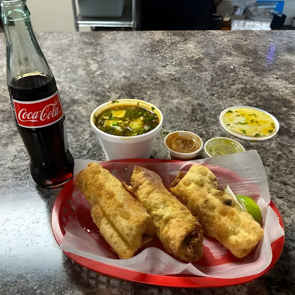Three golden-brown flautas in a red basket with lime, a Coca-Cola, and three dipping sauces.
