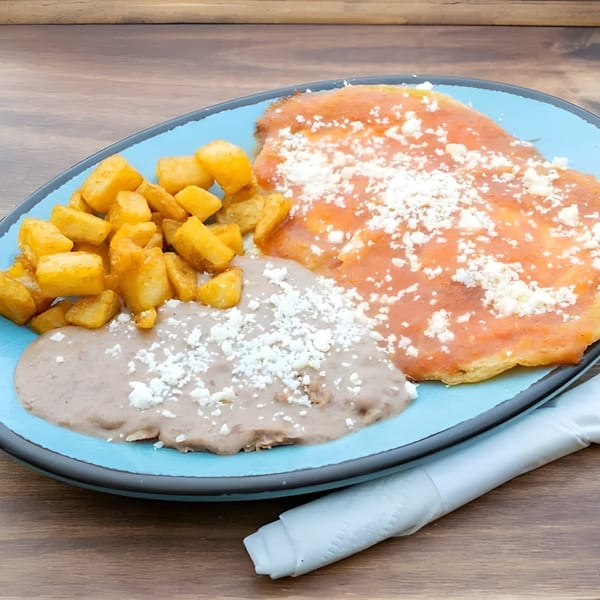 Mexican breakfast plate with enchiladas, refried beans, and home fries on a blue plate.